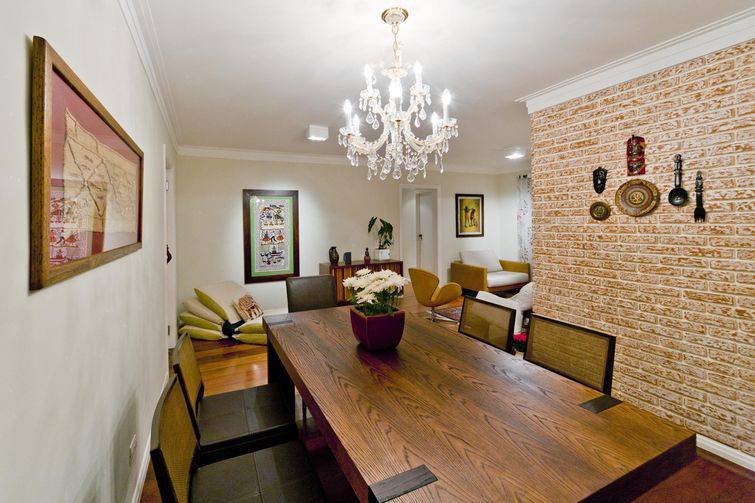 Sala de jantar com revestimentos retrô: parede em tijolo falso, piso de madeira e mesa rústica.