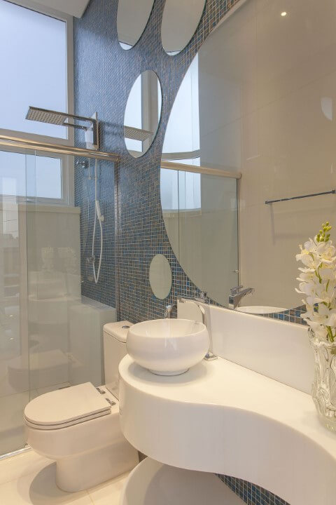 Banheiros decorados com pastilhas azuis e espelhos redondos Projeto de Iara Kilaris