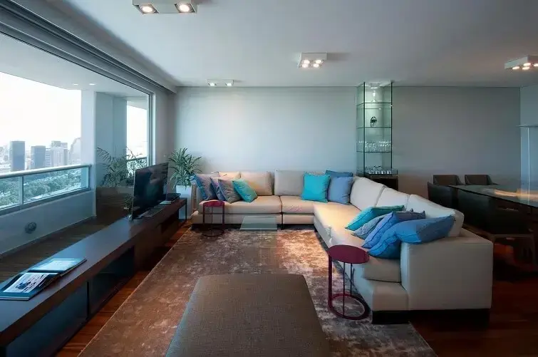 Apartamento amplo com sofá de canto branco e almofadas em tons de azul