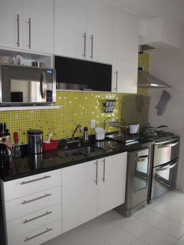 Cozinha pequena com pastilhas amarelas, armários brancos e bancada de granito preto absoluto Projeto de Mariane Battaglia