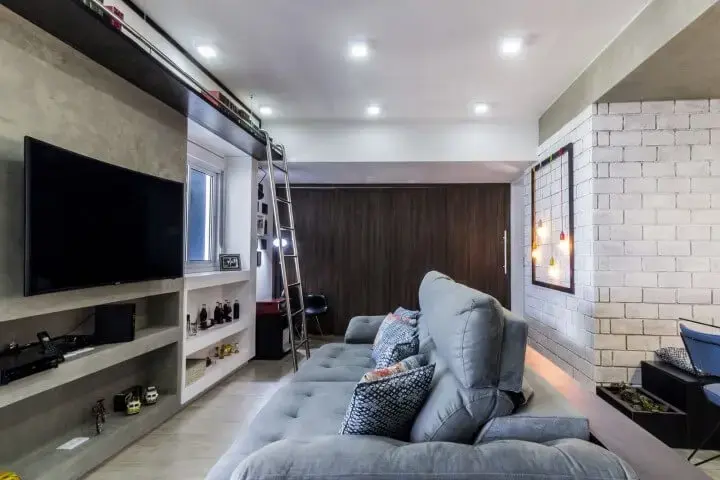 Sala de TV com painel de cimento queimado combinando com sofá cinza Projeto de Andre Freitas
