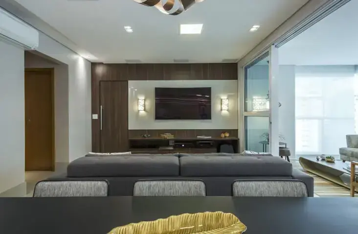 Sala de TV com painel de vidro branco e iluminação aos lados Projeto de Arquiteta Petini