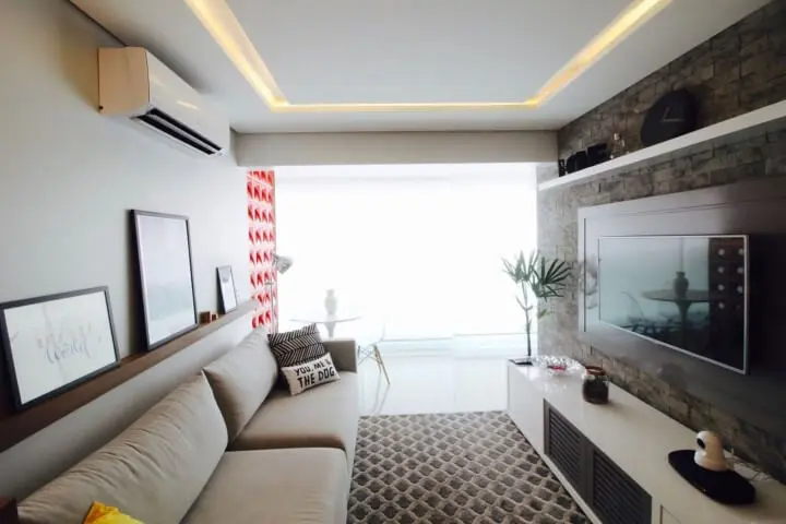 Sala de TV com parede de tijolos e prateleiras acima da TV e do sofá Projeto de Gláucio Gonçalves