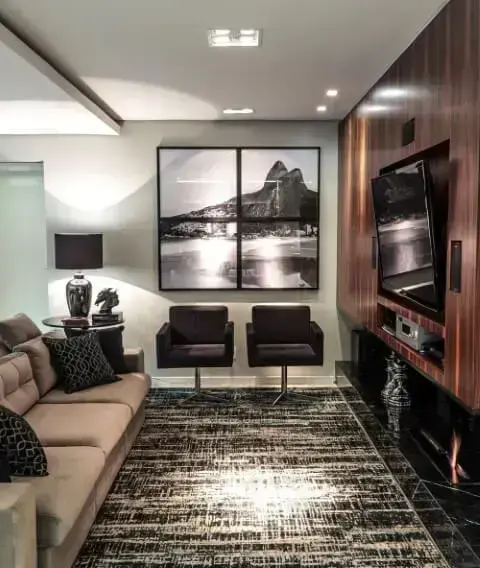 Sala de TV com parede revestida em madeira e TV adaptável Projeto de Pauline Feoni