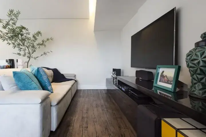 Sala de TV com sofá branco e chão de madeira rústica