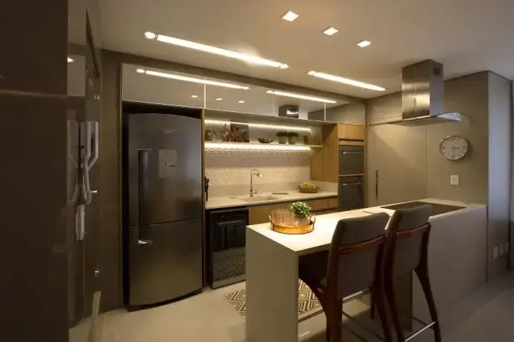 Cozinha americana com revestimento 3D em parte da parede com iluminação embutida Projeto de Marina Turnes
