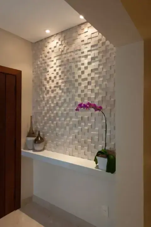 Hall com meia parede com revestimento 3D e iluminação focada Projeto de Bernal Projetos