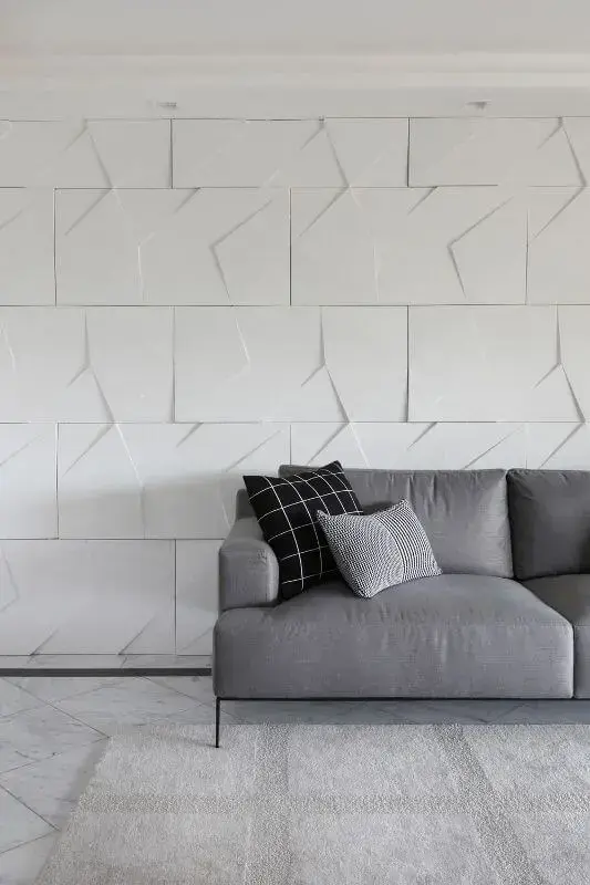 Sala de estar com parede com revestimento 3D atrás do sofá Projeto de Bianchi Lima
