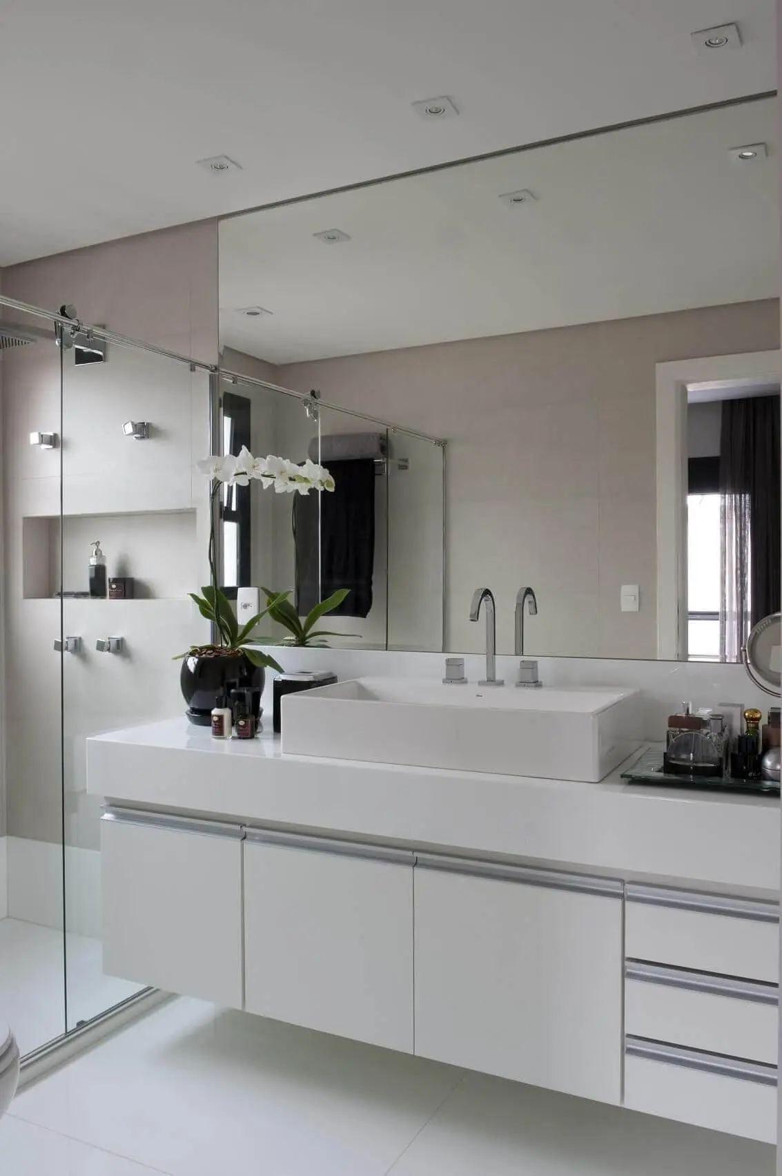 Decoração de banheiro com espelho amplo, gabinete com portas e gavetas e nicho Projeto de Jamile