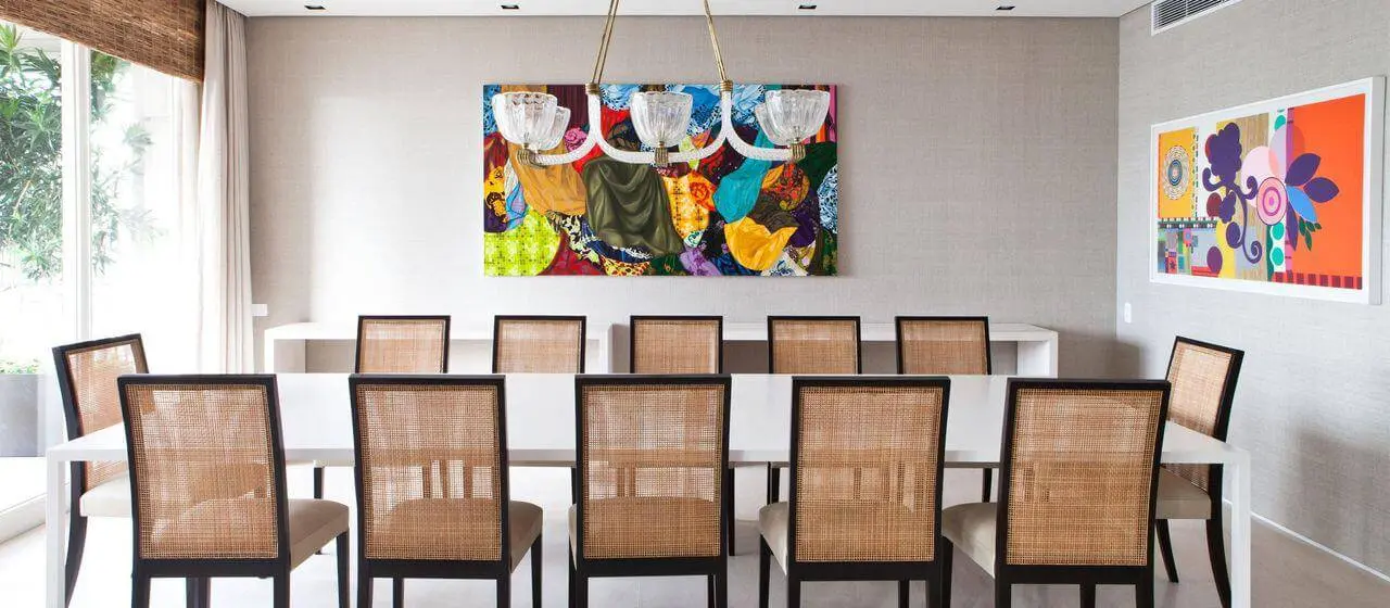 Decoração simples em sala de jantar com mesas brancas e quadros coloridos Projeto de Olegario de Sá