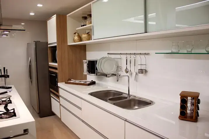 Cozinha planejada com móveis brancos, detalhe em madeira e vidro branco Projeto de Larissa