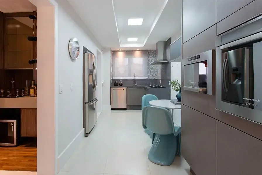 Cozinha planejada em corredor com armários cinzas combinando com os eletrodomésticos em inox Projeto de Marcia Acaro