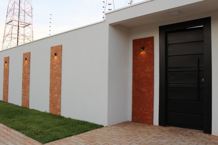 Frente de casas com muro branco e detalhes de tijolos aparentes Projeto de Bianca Monteiro