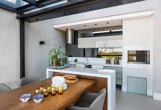 Casa com varanda gourmet com mesa de madeira e poltronas Projeto de Leonardo Muller