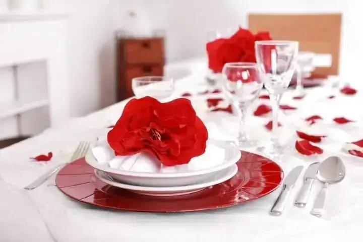 Sousplat vermelho em mesa com flores e pétalas vermelhas