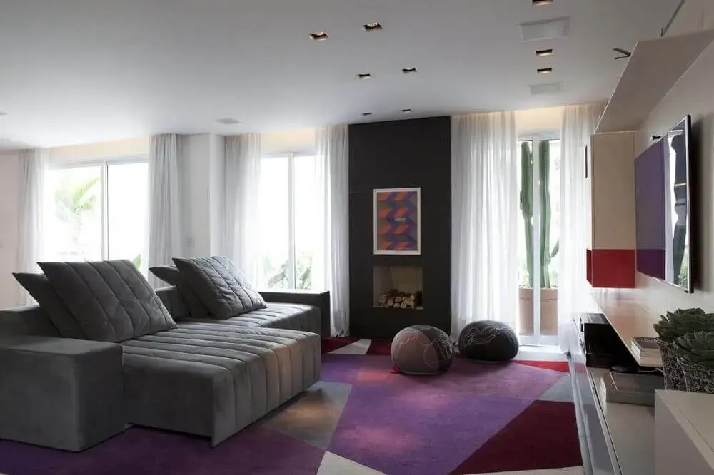 sala com sofá retrátil cinza e tapete em tons de roxo e lilás