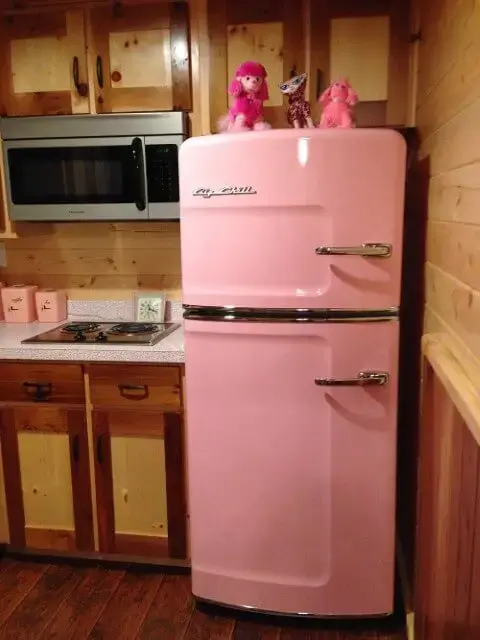 Geladeira colorida cor de rosa em cozinha com móveis de madeira