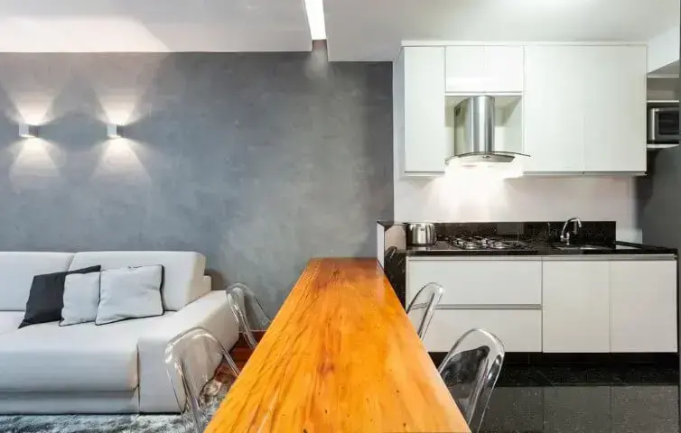 Loft com cozinha americana ligada à sala por uma mesa de madeira Projeto de Laura Santos