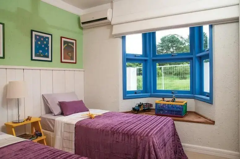 Quarto de solteiro com parede verde e janela azul com cama box separada do colchão Projeto de Rico Mendonça