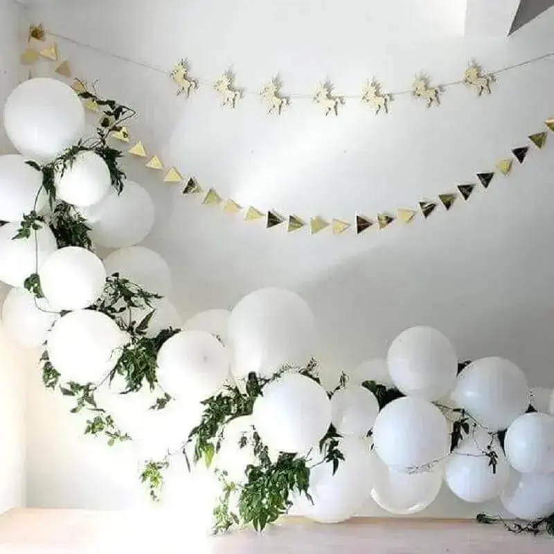 decoração para festa com varal de unicórnios e painel de balões brancos com folhagens Foto Allegro
