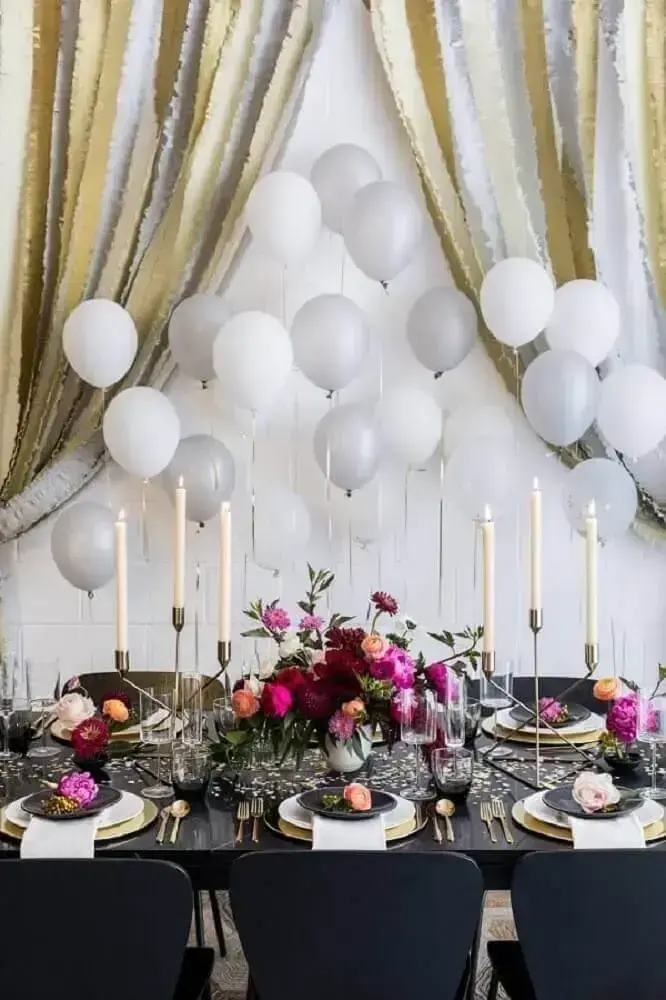 decoração sofisticada para festa com painel de balões prata e branco com muitos arranjos de flores sobre a mesa e castiçais Foto Crate and Barrel