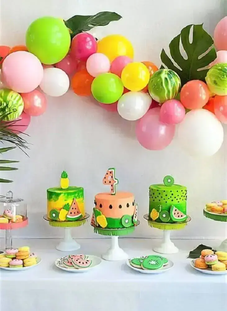 festa tropical decorada com painel de balões coloridos folhagens e bolos diferentes Foto Pinterest