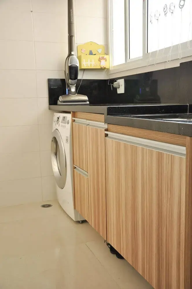 lavanderia planejada com bancada preta e armários que imitam madeira Foto DECORELLAS