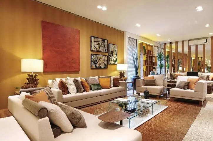 Decoração de sala sofisticada com parede dourada e várias almofadas coloridas Projeto de Quitete Faria