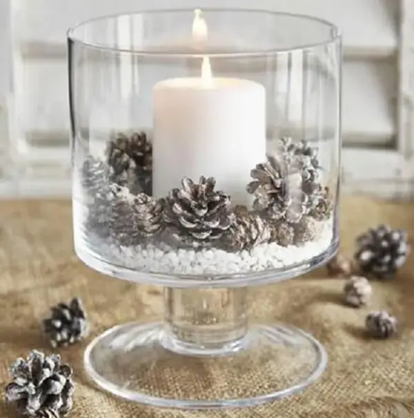 Pote de vidro, pinhas e vela branca compõe a decoração do centro de mesa