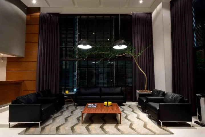 Jogo com três exemplares de sofá de couro preto em sala com o pé direito alto Projeto de Rafael Guimarães