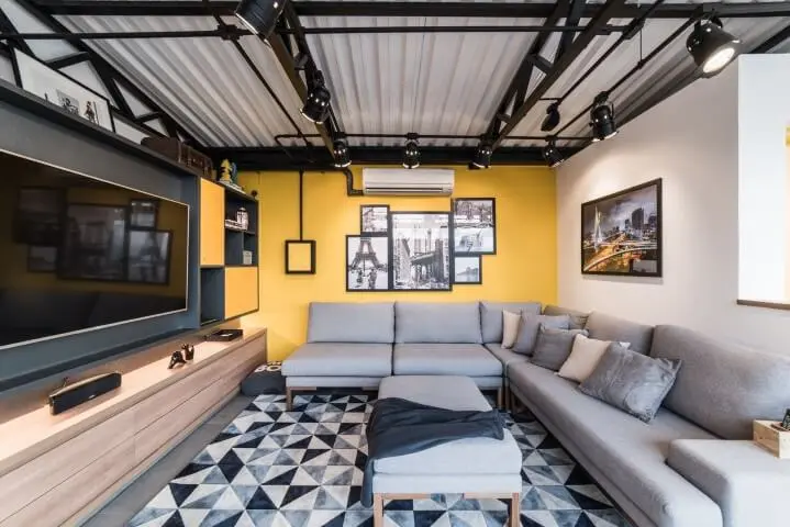 Sala com parede amarela e sofá em L cinza e tapete geométrico Projeto de Pietro Terlizzi