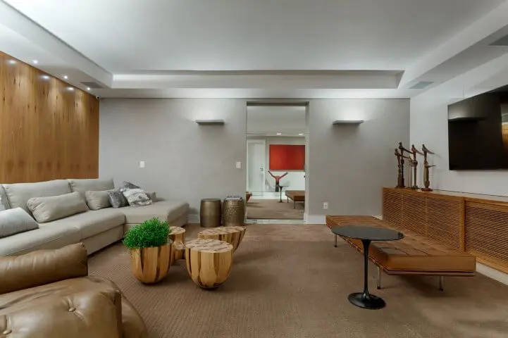 Sala de TV com decoração aconchegante, sofá em L claro e demais móveis em tons de marrom e madeira Projeto de Jaqueline Frauches