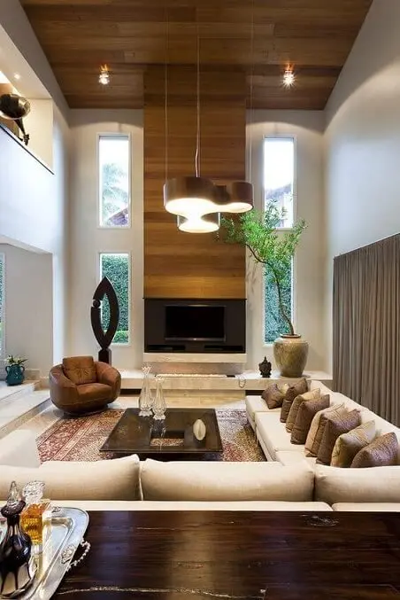 Sala de TV com pé direito duplo e sofá em L com várias almofadas Projeto de Marlúcia Landim Decor