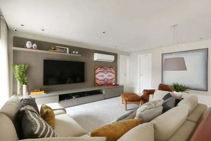 Sala de TV com sofá em L claro e almofadas diversas Projeto de Karen Pisaca