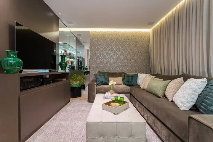 Sala de TV com sofá em L escuro combinando com rack marrom Projeto de Helena Koki