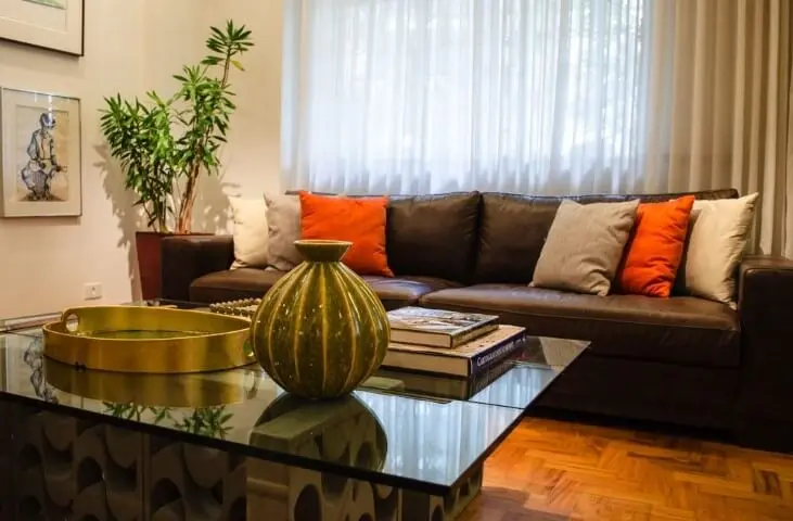 Sala de estar com mesa de centro de vidro com cobogós e sofá de couro marrom com almofadas Projeto de Adriana Fornazari