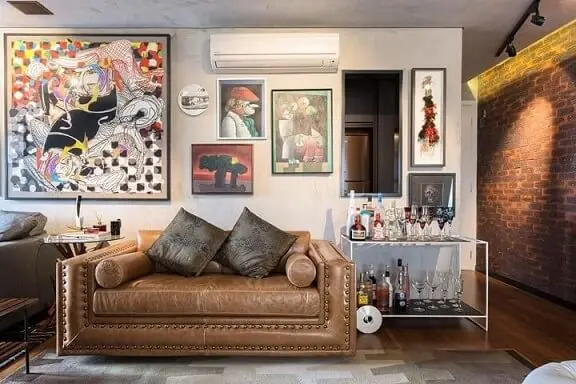 Sala de estar com quadros divertidos sobre o sofá de couro marrom claro Projeto de Clarice Semerene