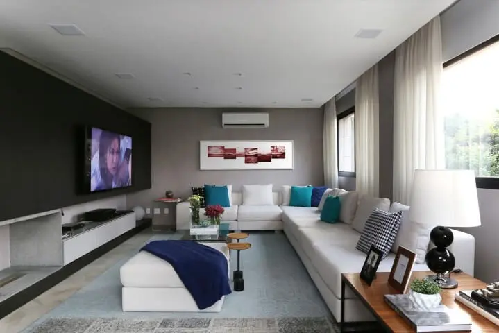 Sala de estar com sofá de canto branco e almofadas em tons de azul Projeto de Hildebrand Silva Arquitetura