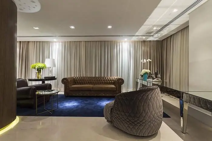 Sala de estar com sofá de couro marrom e poltronas grandes Projeto de Mauricio Karam