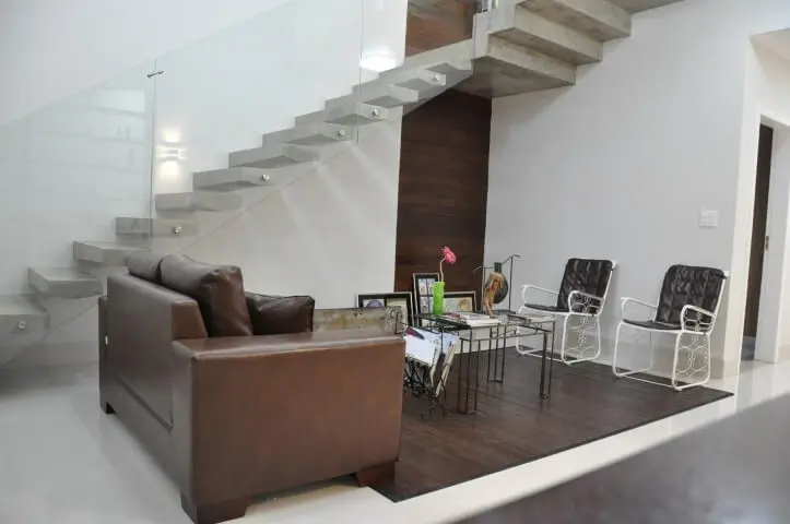 Sala de estar com sofá de couro pequeno marrom claro com cadeiras brancas Projeto de Pedro Haruf