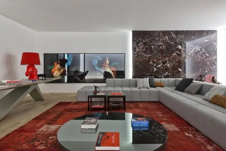 Sala de estar com sofá em L cinza amplo e tapete vermelho Projeto de Casa Cor 2016