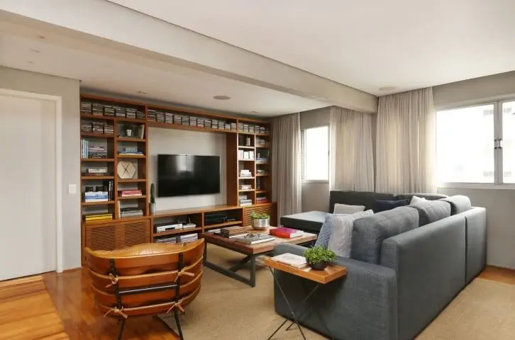 Sala de estar com sofá em L cinza e demais móveis de madeira Projeto de Oliveira Arquitetura