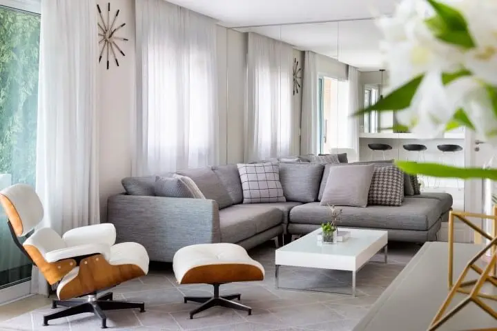 Sala de estar com sofá em L cinza e poltrona Eames branca Projeto de GF Projetos