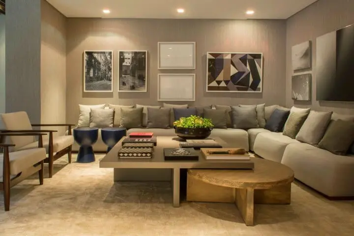Sala de estar com sofá em L e várias almofadas e quadros decorativos Projeto de Triplex Arquitetura
