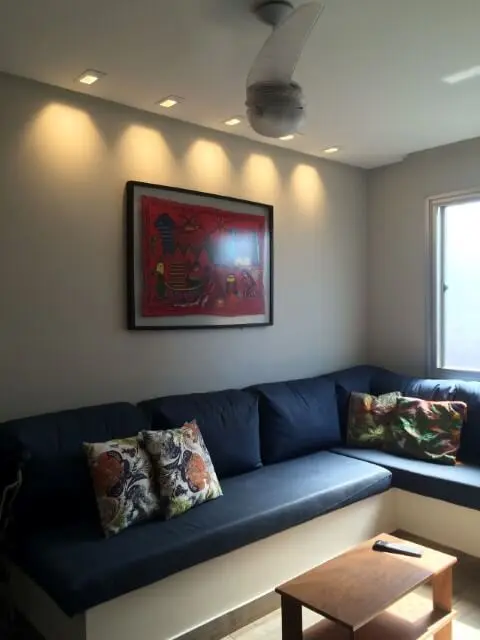 Sala de estar de apartamento com sofá em L com almofadas azuis Projeto de Lizandra Zagoto