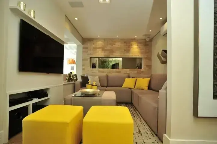 Sala de estar pequena com sofá em L bege e puffs e almofadas amarelas Projeto de Renata Tolentino