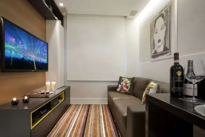 Sala de estar pequena com sofá de couro, tapete listrado colorido e painel para TV de madeira Foto de Eduardo Imóveis