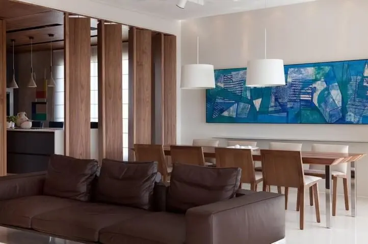 Sala integrada com sofá de couro escuro e mesa longa de madeira Projeto de Patricia Martinez
