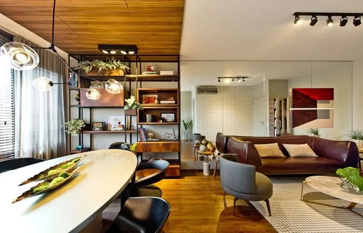 Sala integrada com sofá de couro escuro e poltrona cinza Projeto de Espaço do Traço