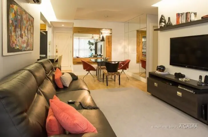 Sala integrada com sofá de couro preto e almofadas vermelhas Projeto de Rico Mendonça